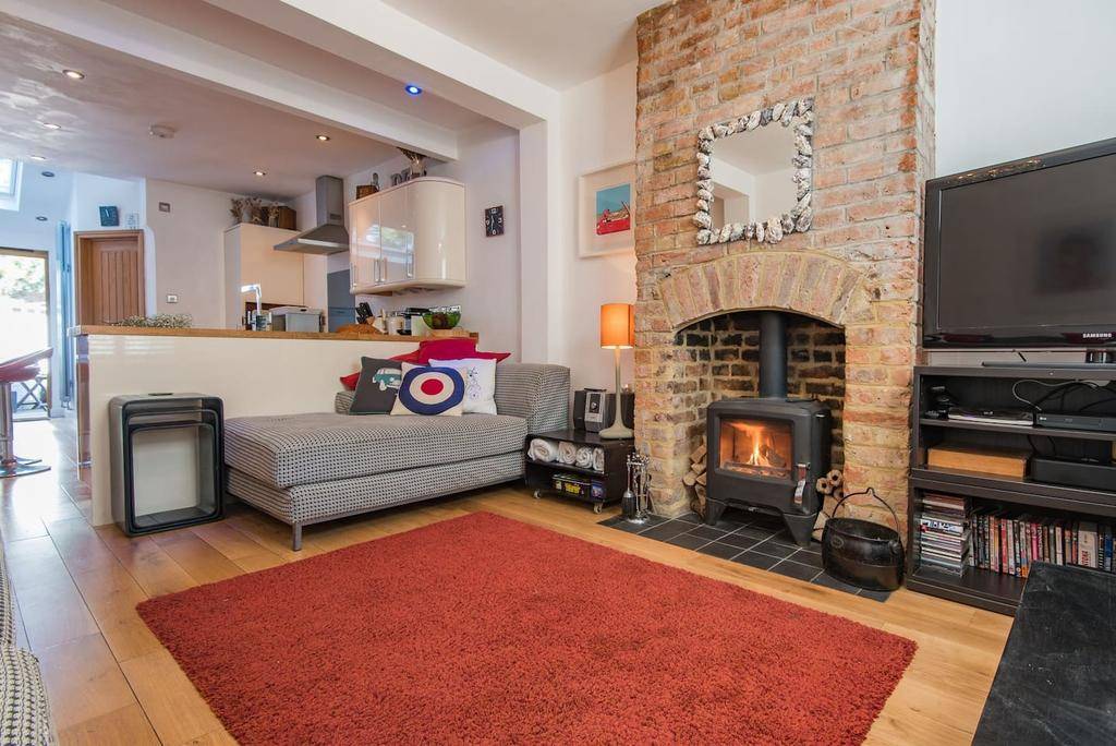 A living room with a wooden floor, red carpet and brick fireplace with a roaring fire