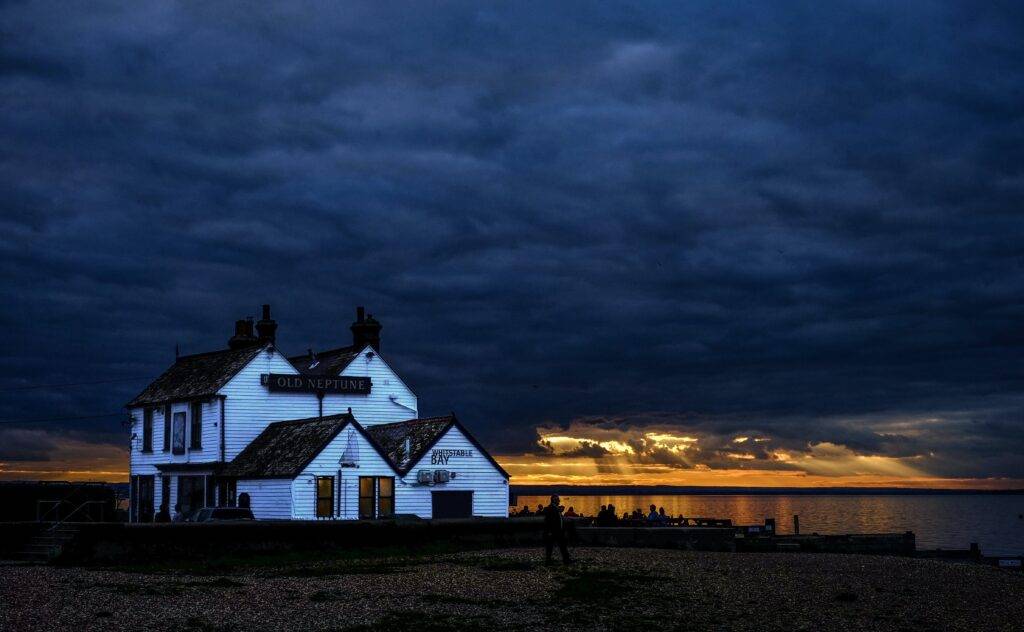 A white pub on a pebbled beach against a dark and cloudy sky