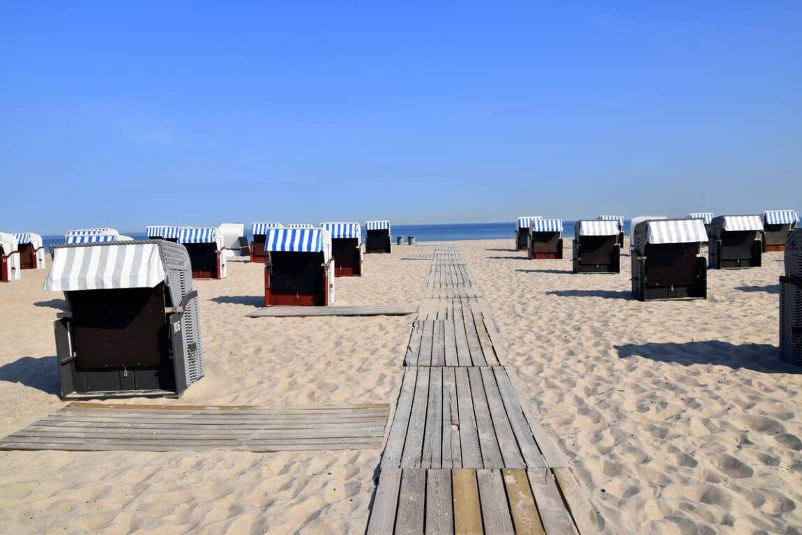 A view towards the sea from the beach, with a wooden walkway down the middle and striped beach baskets on either side