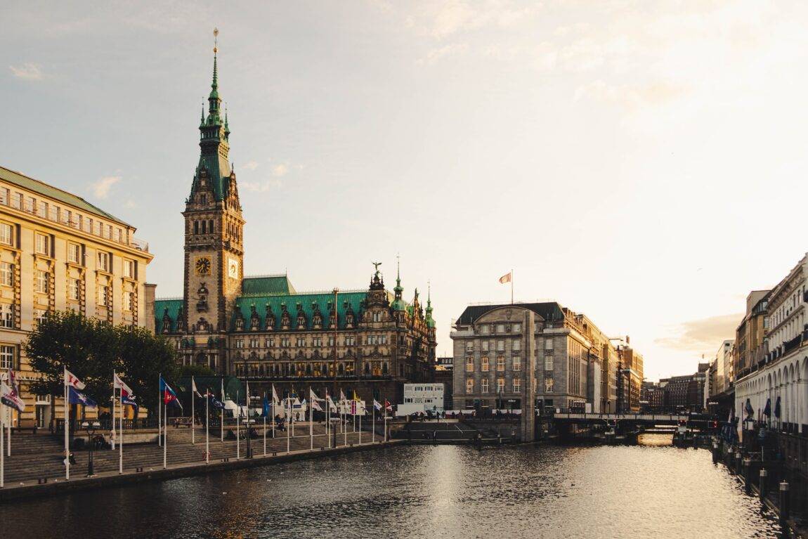 Buildings including Hamburg city hall with a lake in the foreground and flags lining the water