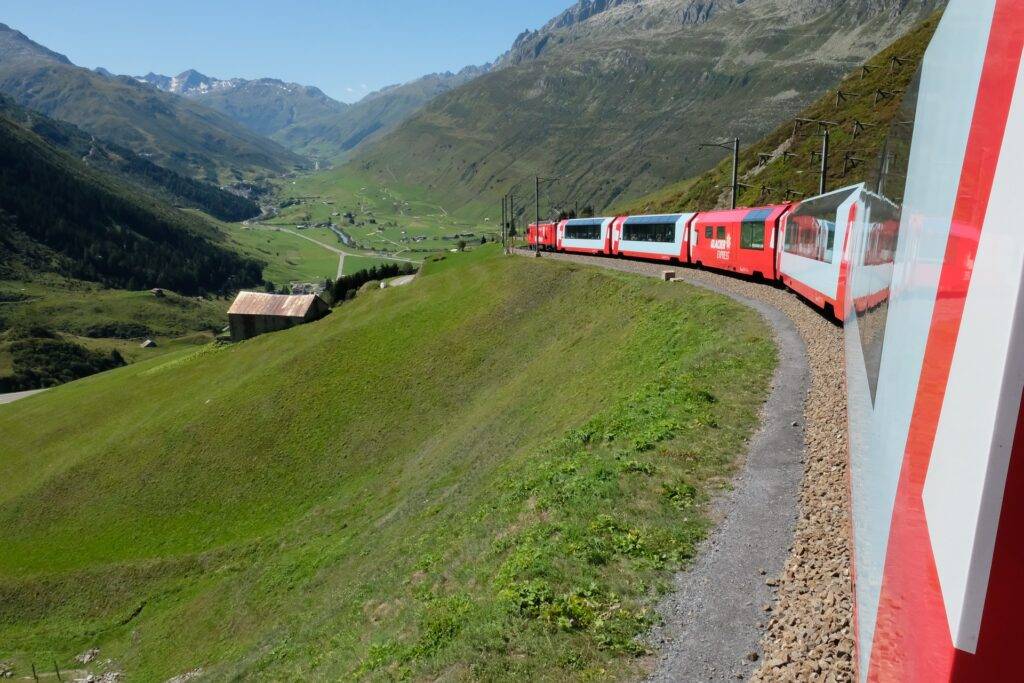 A train travelling through grass-covered  mountains